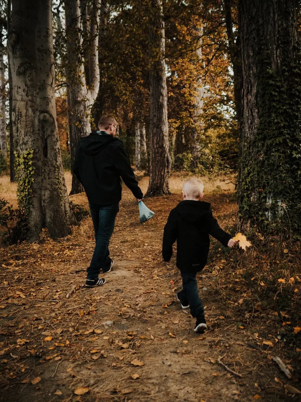 A father and child walking through a wooded path in autumn